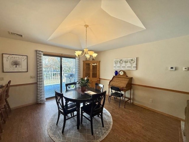 dining space with visible vents, a tray ceiling, wood finished floors, an inviting chandelier, and baseboards