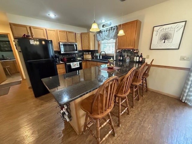 kitchen with wood finished floors, a breakfast bar, a peninsula, a sink, and stainless steel appliances