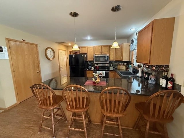 kitchen featuring pendant lighting, a sink, dark countertops, appliances with stainless steel finishes, and a peninsula