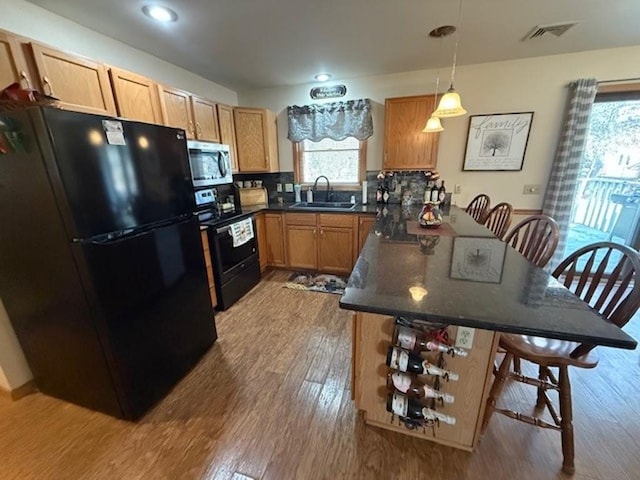 kitchen with visible vents, a peninsula, a sink, black appliances, and a kitchen breakfast bar