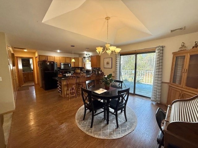 dining space with visible vents, wood finished floors, lofted ceiling, and a chandelier