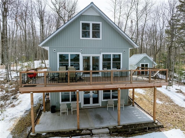 snow covered rear of property featuring a deck, french doors, and a patio