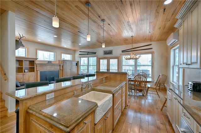 kitchen featuring an AC wall unit, an island with sink, a wealth of natural light, light wood-style flooring, and a sink