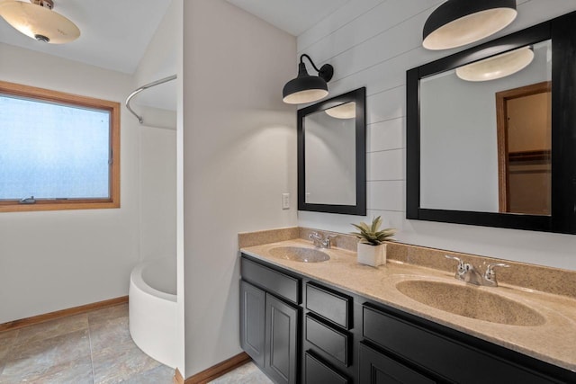 bathroom with double vanity, a tub to relax in, baseboards, and a sink