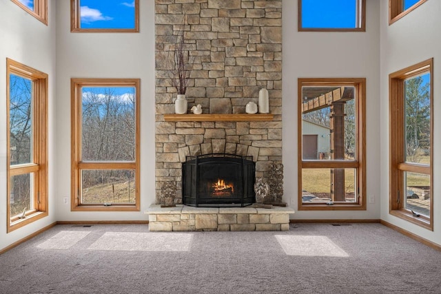 unfurnished living room featuring carpet flooring, a fireplace, a high ceiling, and baseboards