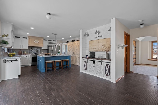 kitchen with backsplash, a barn door, appliances with stainless steel finishes, arched walkways, and white cabinets