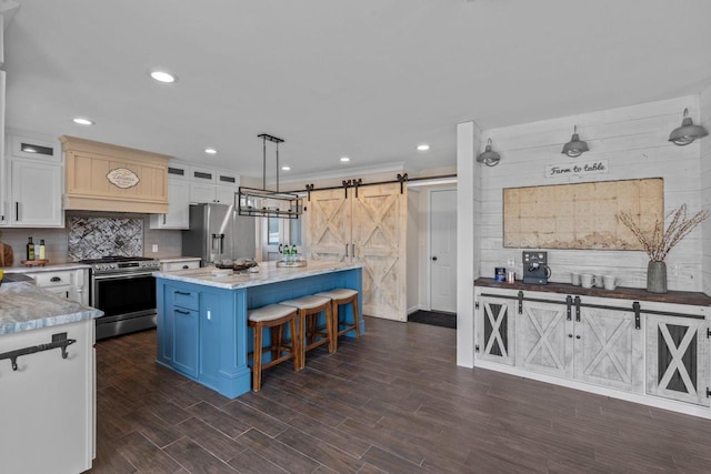 kitchen featuring dark wood finished floors, stainless steel appliances, decorative backsplash, a barn door, and a kitchen breakfast bar