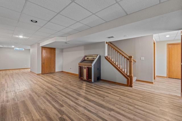 finished below grade area with visible vents, wood finished floors, stairway, baseboards, and a paneled ceiling