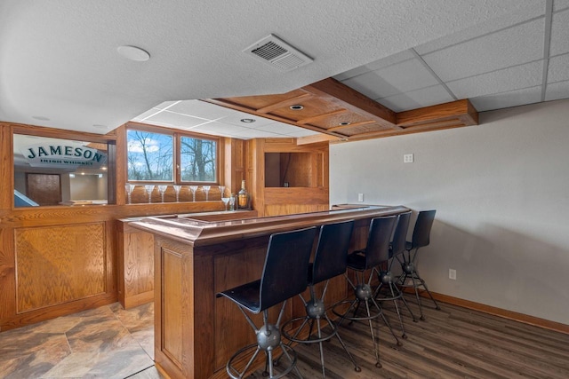 bar featuring visible vents, light wood-style flooring, a drop ceiling, a bar, and baseboards