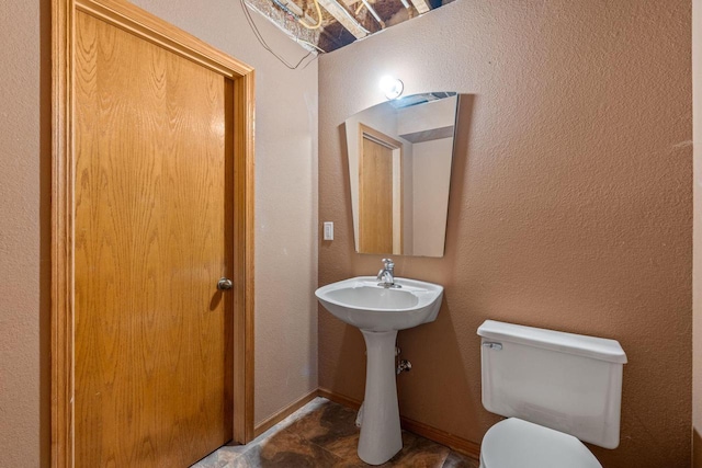 half bathroom with toilet, baseboards, and a textured wall