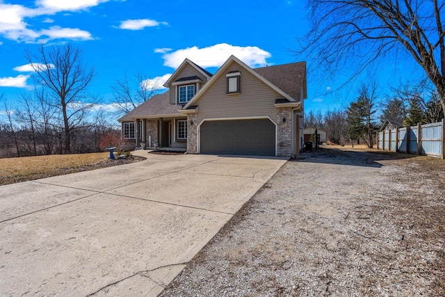 view of front of house with stone siding, an attached garage, concrete driveway, and fence