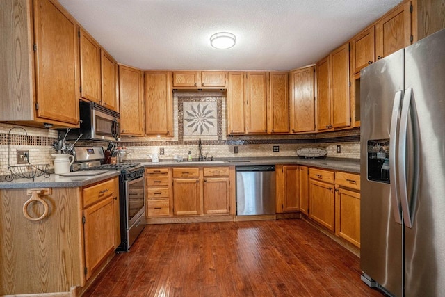 kitchen with brown cabinets, dark wood-type flooring, a sink, tasteful backsplash, and stainless steel appliances