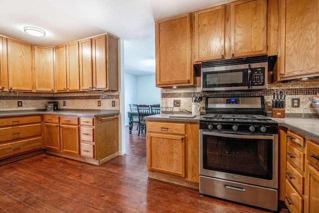 kitchen featuring stainless steel appliances, tasteful backsplash, dark countertops, and dark wood-style floors