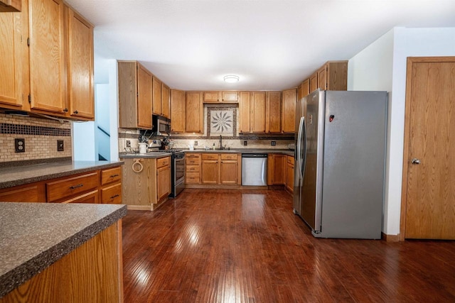 kitchen with dark wood-style flooring, stainless steel appliances, decorative backsplash, and a sink