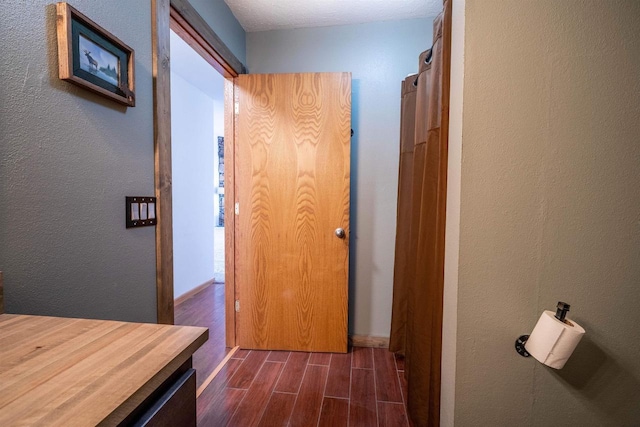 hallway with a textured wall, baseboards, and wood tiled floor