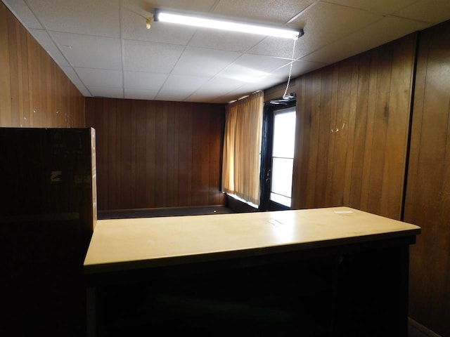 kitchen featuring a drop ceiling, wooden walls, and freestanding refrigerator