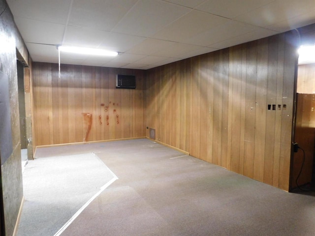 finished basement featuring wood walls, a paneled ceiling, and carpet floors