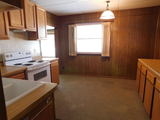 kitchen with tasteful backsplash, wood walls, light countertops, electric stove, and a sink