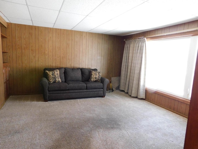 living area featuring a drop ceiling, carpet flooring, and wood walls