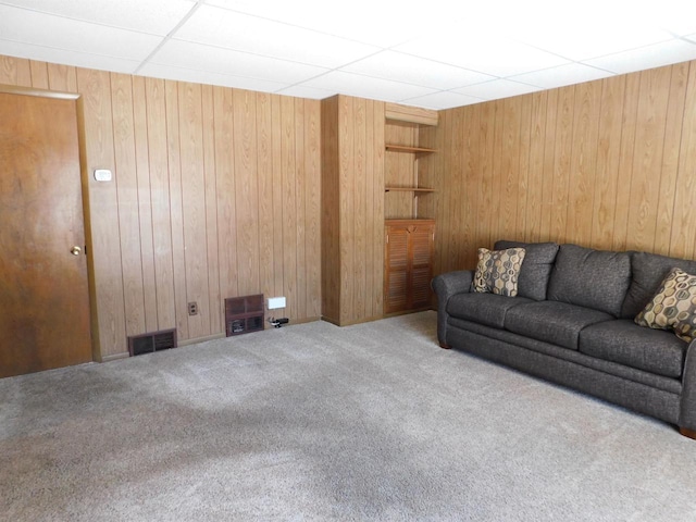 carpeted living room featuring visible vents and wooden walls