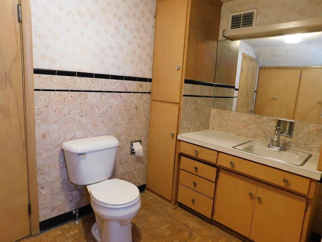 bathroom featuring visible vents, wallpapered walls, toilet, wainscoting, and vanity