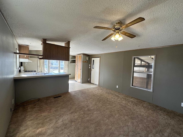 unfurnished living room featuring light carpet, visible vents, a textured ceiling, and a ceiling fan