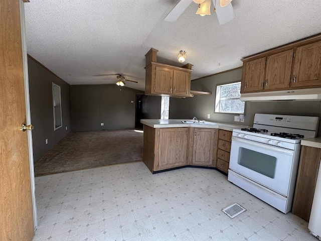 kitchen featuring under cabinet range hood, gas range gas stove, open floor plan, a peninsula, and light floors