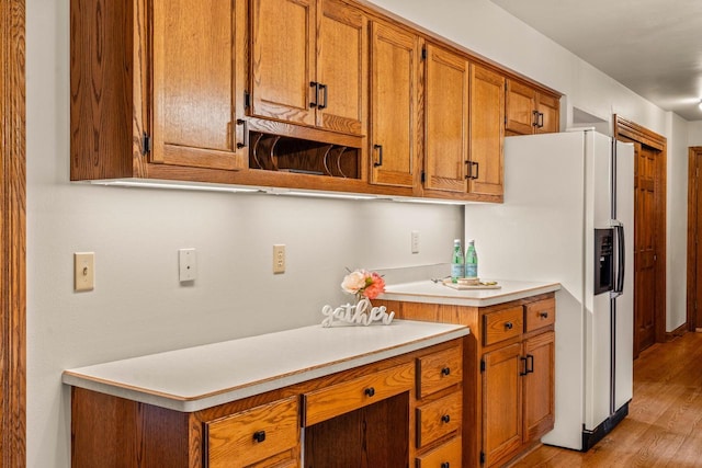 kitchen featuring light wood-style floors, white fridge with ice dispenser, brown cabinetry, and light countertops