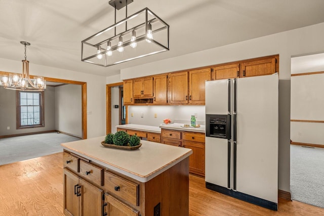 kitchen with a kitchen island, light countertops, hanging light fixtures, white fridge with ice dispenser, and brown cabinetry