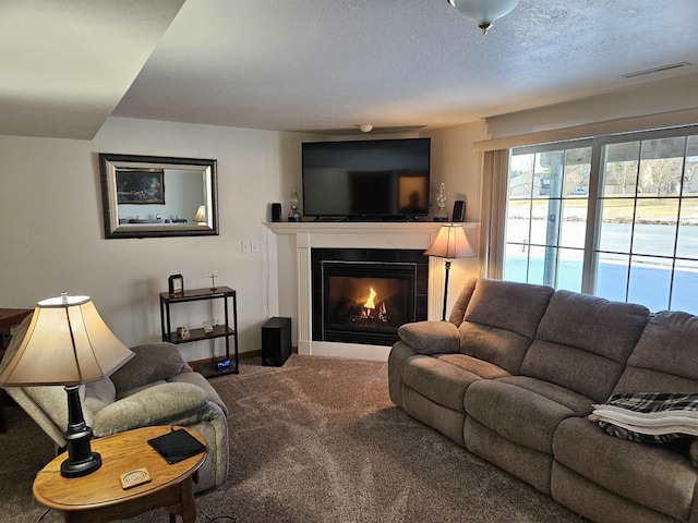 living area with visible vents, baseboards, carpet, a glass covered fireplace, and a textured ceiling