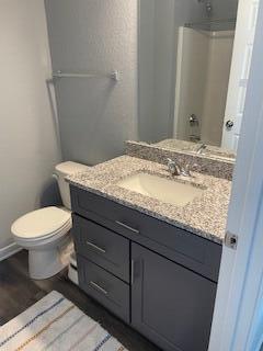 full bath featuring vanity, wood finished floors, baseboards, walk in shower, and toilet