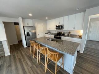 kitchen with dark wood-style floors, a breakfast bar area, white cabinetry, and stainless steel appliances