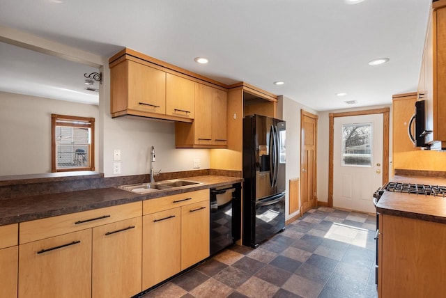 kitchen with black appliances, light brown cabinetry, a sink, dark countertops, and recessed lighting