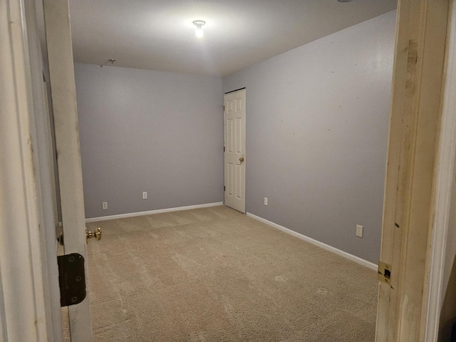 spare room featuring light colored carpet and baseboards