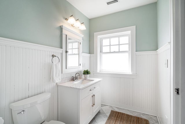 half bath featuring a wainscoted wall, toilet, and visible vents