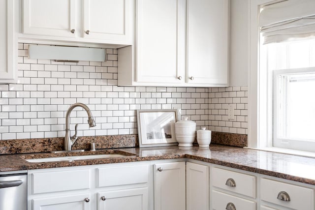 kitchen with tasteful backsplash, dishwasher, dark stone countertops, white cabinets, and a sink