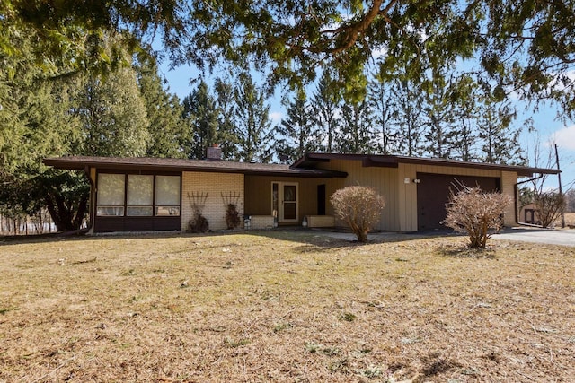 mid-century modern home featuring brick siding, a front yard, a chimney, a garage, and driveway