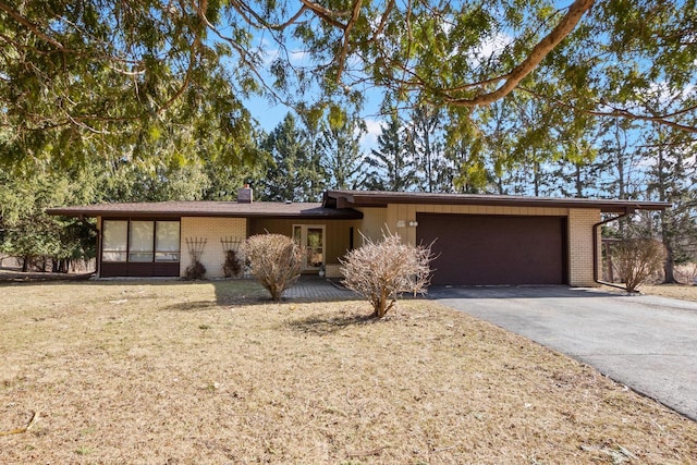 mid-century modern home featuring an attached garage, brick siding, driveway, and a chimney