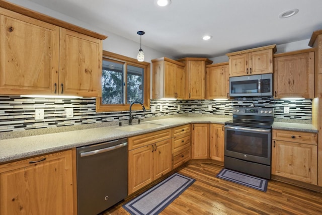 kitchen featuring pendant lighting, light countertops, wood finished floors, stainless steel appliances, and a sink