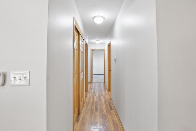 hall featuring light wood-style flooring and baseboards