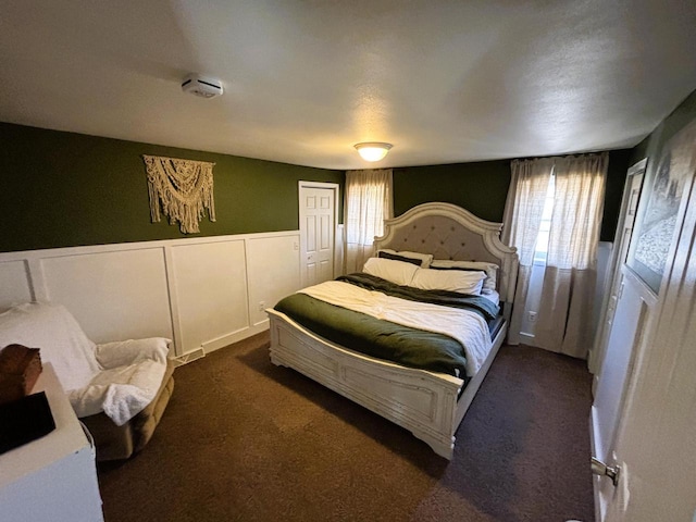 bedroom featuring a wainscoted wall and dark colored carpet