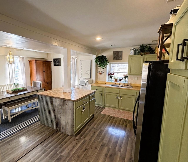 kitchen with dark wood-style floors, green cabinetry, freestanding refrigerator, a sink, and wood counters