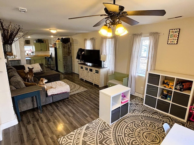 living room with visible vents, baseboards, dark wood-type flooring, and ceiling fan