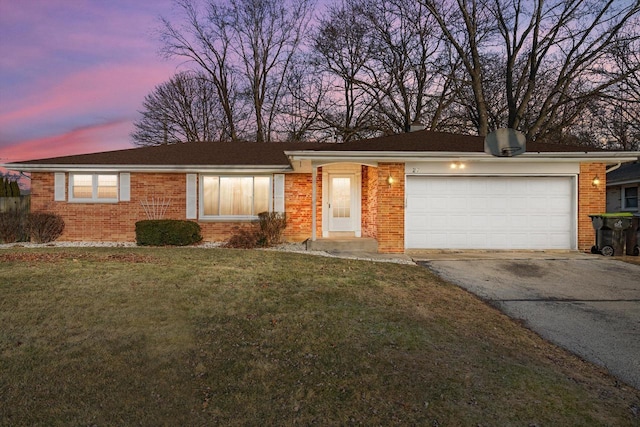 single story home featuring aphalt driveway, a garage, a yard, and brick siding