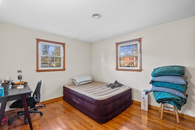 bedroom featuring visible vents, multiple windows, baseboards, and wood finished floors