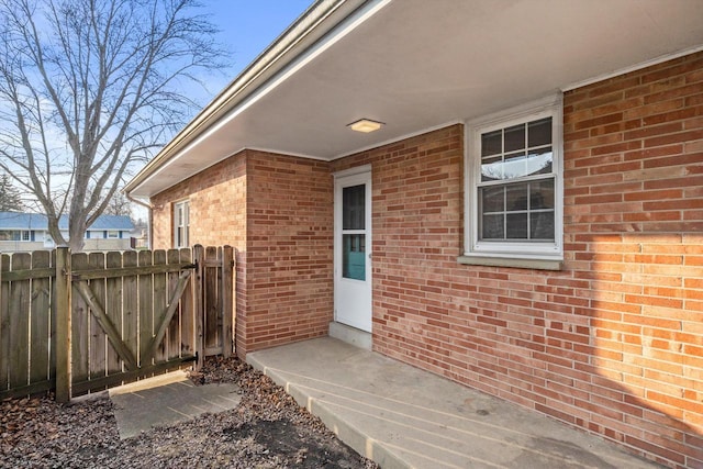 view of exterior entry featuring brick siding, a gate, and fence