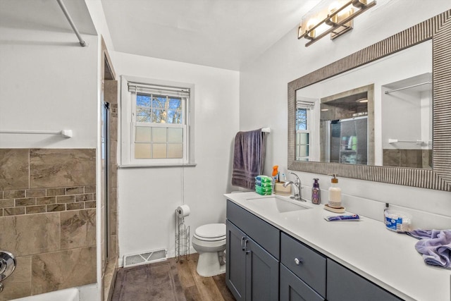 bathroom with visible vents, toilet, a tile shower, wood finished floors, and vanity