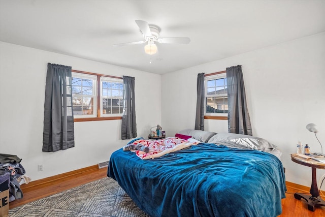 bedroom with a ceiling fan, wood finished floors, visible vents, and baseboards