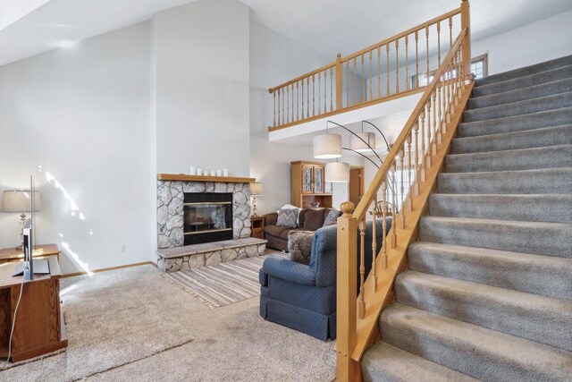 living room featuring stairway, carpet, baseboards, high vaulted ceiling, and a stone fireplace