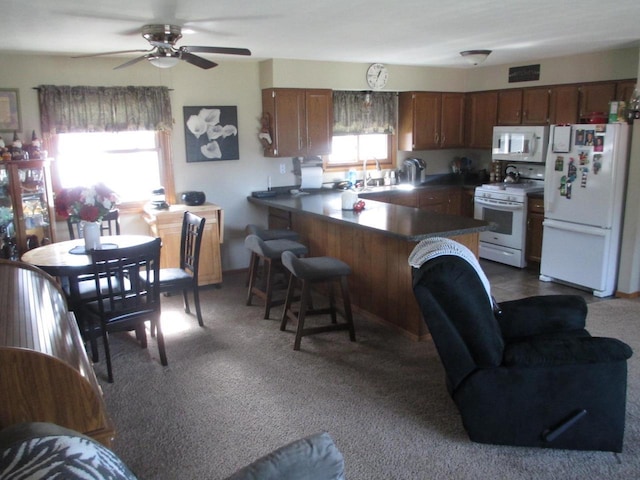 kitchen featuring a kitchen bar, a sink, white appliances, a peninsula, and dark colored carpet